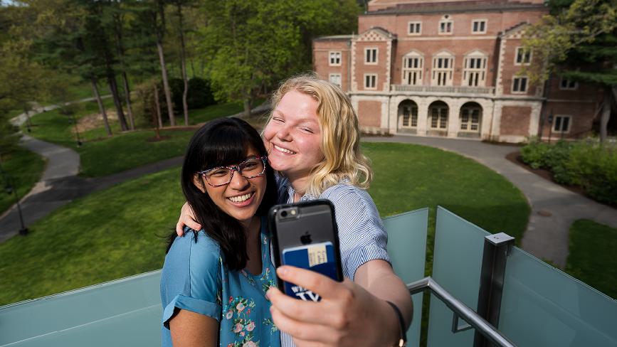 Two Wellesley College students take a selfie in front of Diana Champman Walsh Alumnae Hall