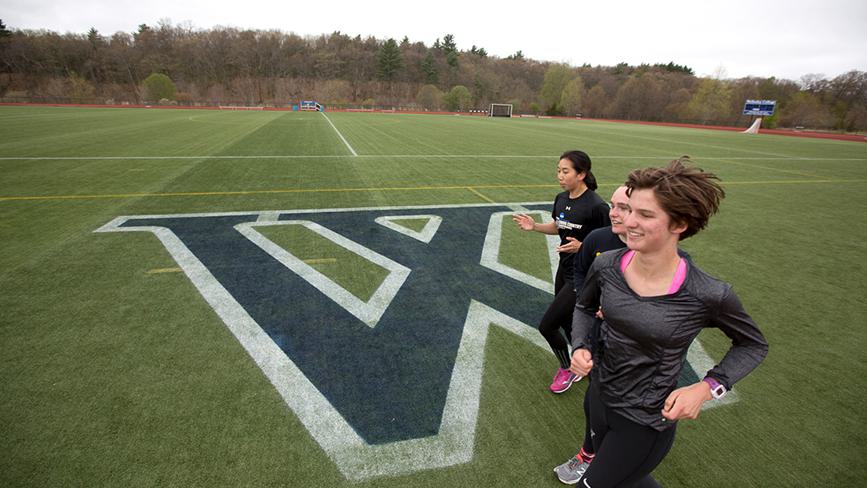 Wellesley student athletes run on a sports field with the Wellesley logo