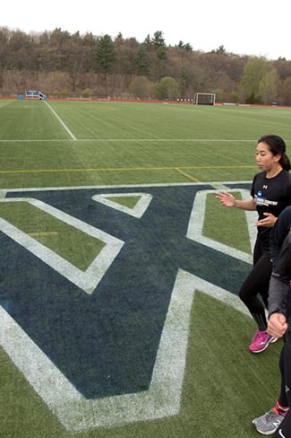 Wellesley student athletes run on a sports field with the Wellesley logo