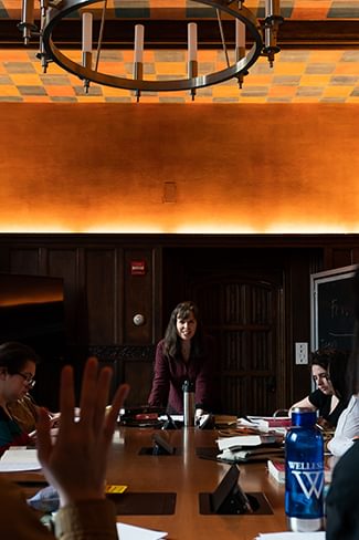 A Wellesley College student raises her hand in a seminar class while professor looks on