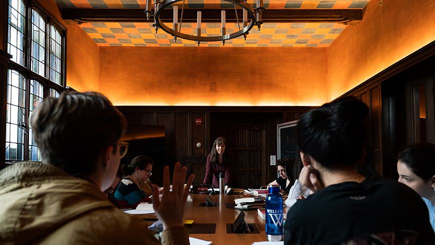 A Wellesley College student raises her hand in a seminar class while professor looks on