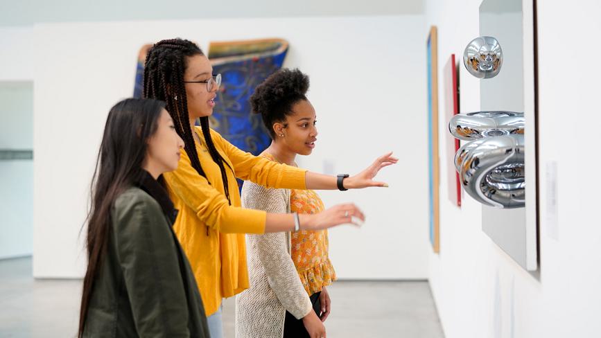A Wellesley College student leads a tour of two other students through the Davis Museum, explaining an art installation