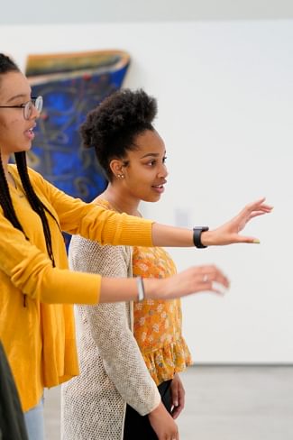 A Wellesley College student leads a tour of two other students through the Davis Museum, explaining an art installation