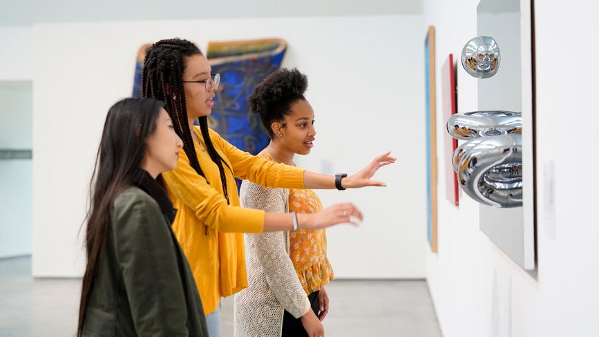 A Wellesley College student leads a tour of two other students through the Davis Museum, explaining an art installation