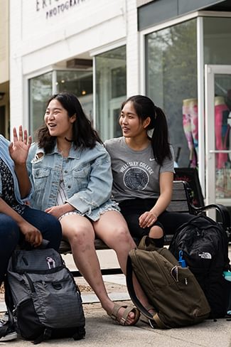 Four college students laugh on a bench in downtown Wellesley
