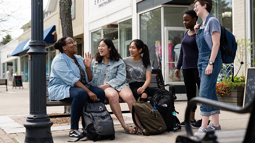 Four college students laugh on a bench in downtown Wellesley