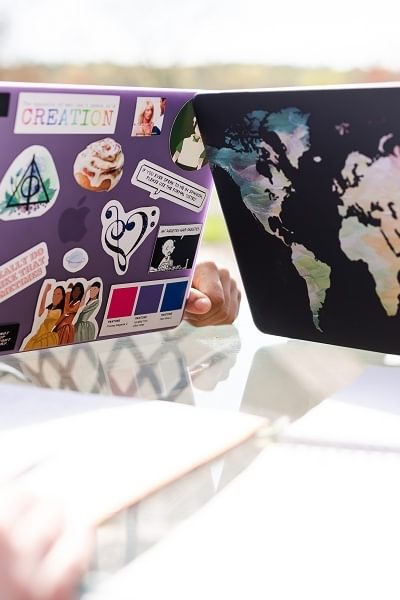 Two students sit at their laptops that are covered with decorative stickers