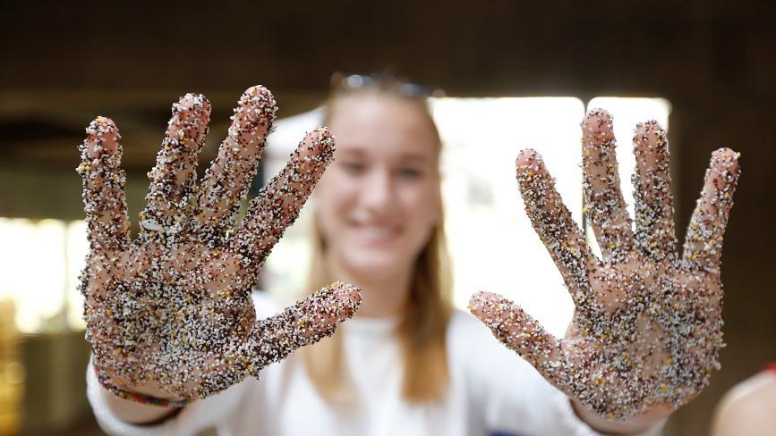 A Wellesley College student holds out her hands in front of her, covered in dyed sand