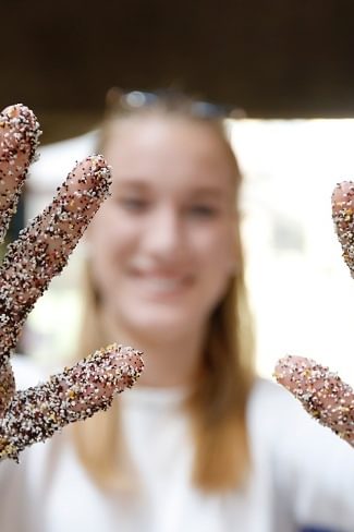 A Wellesley College student holds out her hands in front of her, covered in dyed sand